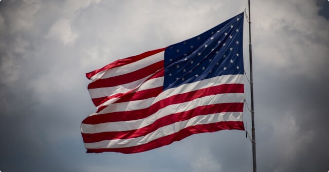 A big US flag with cloudy sky in the background.