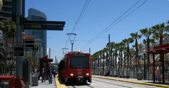 The San Diego trolley approaching a station on a sunny day.